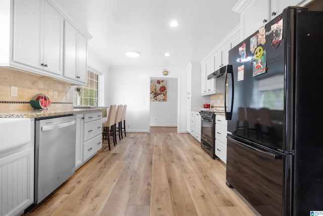 kitchen featuring white cabinetry, light stone counters, tasteful backsplash, light hardwood / wood-style floors, and black appliances