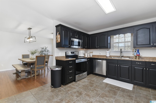 kitchen with stainless steel appliances, hanging light fixtures, stone countertops, a sink, and dark cabinetry