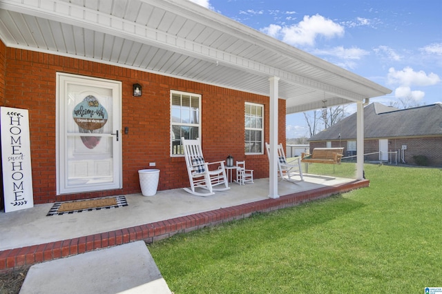 view of exterior entry with covered porch, brick siding, and a yard