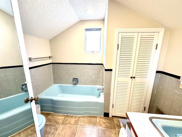 bathroom with tile walls, vanity, a bath, a textured ceiling, and toilet