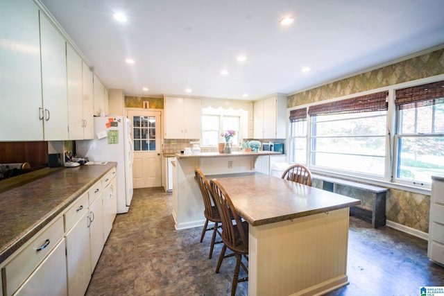 kitchen featuring white refrigerator, a breakfast bar, white cabinets, and a center island