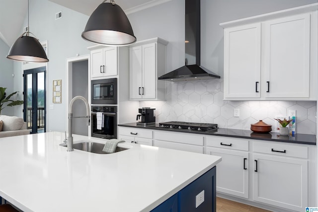 kitchen featuring a sink, black appliances, wall chimney exhaust hood, dark countertops, and decorative light fixtures