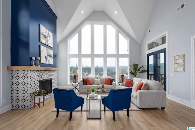 living area with high vaulted ceiling, visible vents, light wood finished floors, and a tiled fireplace