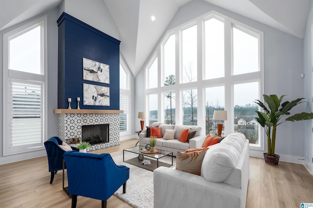 living area featuring baseboards, high vaulted ceiling, a tile fireplace, and light wood-style floors