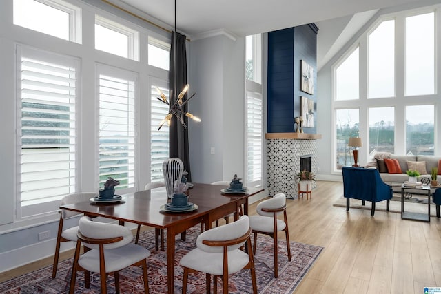 dining space featuring a healthy amount of sunlight, light wood-style flooring, a fireplace, and a towering ceiling