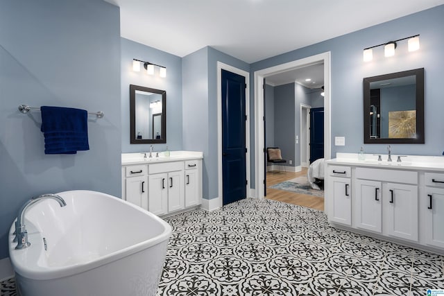 full bathroom featuring a soaking tub, two vanities, a sink, and baseboards