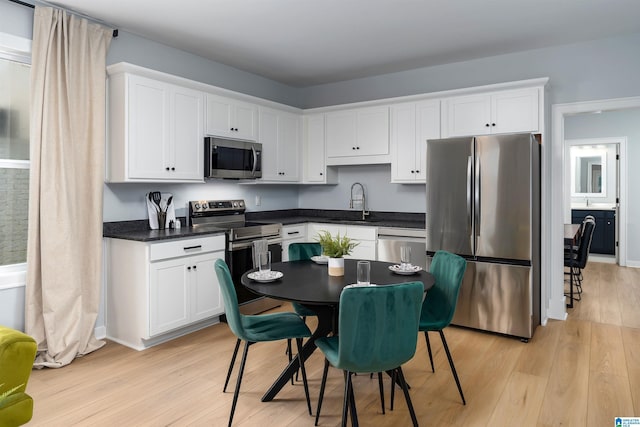 kitchen with stainless steel appliances, dark countertops, white cabinetry, and light wood finished floors