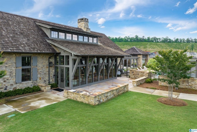 rear view of property featuring a yard, stone siding, a chimney, and a patio