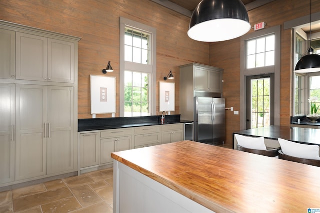 kitchen featuring gray cabinetry, wooden walls, wooden counters, stone finish flooring, and stainless steel fridge