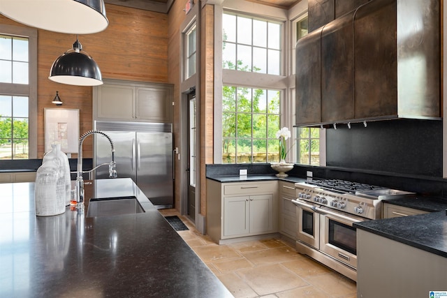 kitchen featuring high end appliances, dark countertops, wooden walls, and a high ceiling