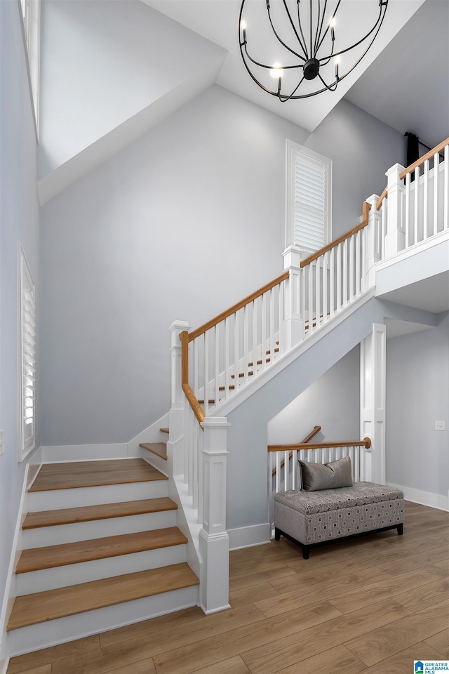 stairs featuring baseboards, a towering ceiling, an inviting chandelier, and wood finished floors