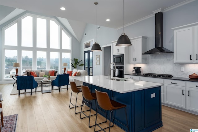 kitchen with open floor plan, decorative light fixtures, stainless steel appliances, wall chimney range hood, and a sink