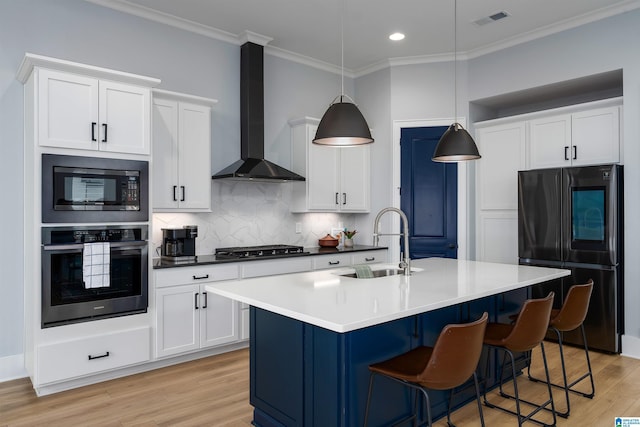 kitchen featuring white cabinets, appliances with stainless steel finishes, hanging light fixtures, wall chimney range hood, and a sink