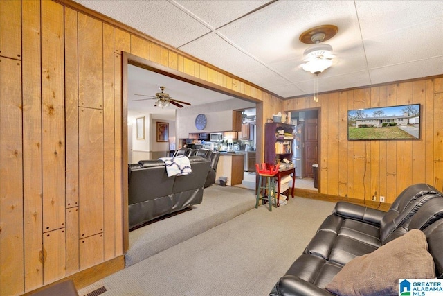 carpeted living room with ceiling fan and wooden walls