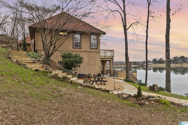 property exterior at dusk with a patio and a water view