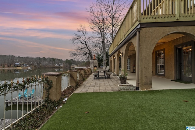 yard at dusk with an outdoor fireplace, a patio, and a water view