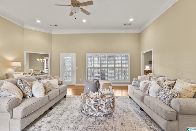 living room featuring ceiling fan with notable chandelier, wood-type flooring, ornamental molding, and a towering ceiling