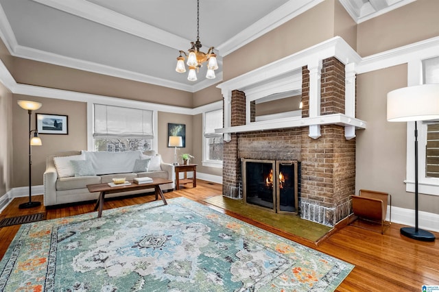 living room featuring hardwood / wood-style flooring, a brick fireplace, crown molding, and a notable chandelier