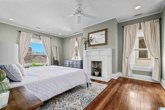 bedroom featuring a brick fireplace, crown molding, ceiling fan, and wood-type flooring