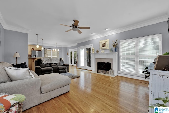 living room with ceiling fan with notable chandelier, ornamental molding, a premium fireplace, and light wood-type flooring