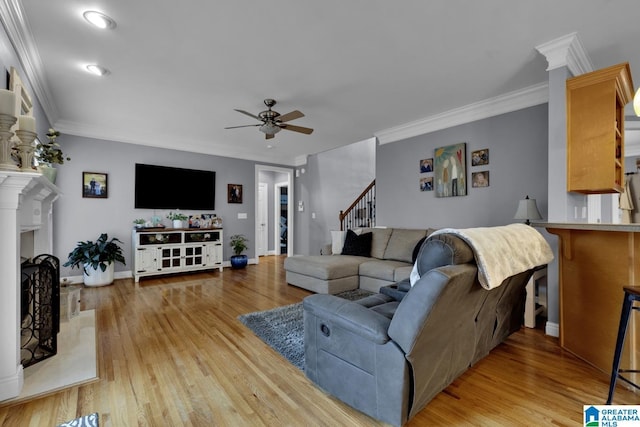 living room with crown molding, ceiling fan, a premium fireplace, and light hardwood / wood-style flooring