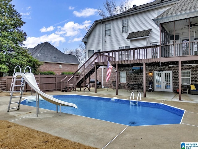 view of swimming pool with ceiling fan, a water slide, a wooden deck, a patio area, and french doors