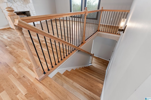 stairs with hardwood / wood-style flooring and a stone fireplace