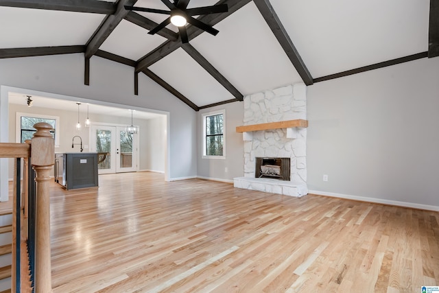 unfurnished living room featuring beam ceiling, a stone fireplace, sink, and light hardwood / wood-style floors