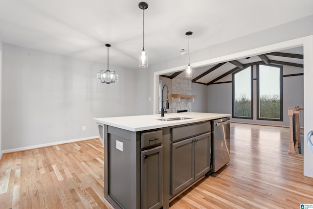 kitchen featuring sink, hanging light fixtures, stainless steel dishwasher, a center island with sink, and light hardwood / wood-style flooring