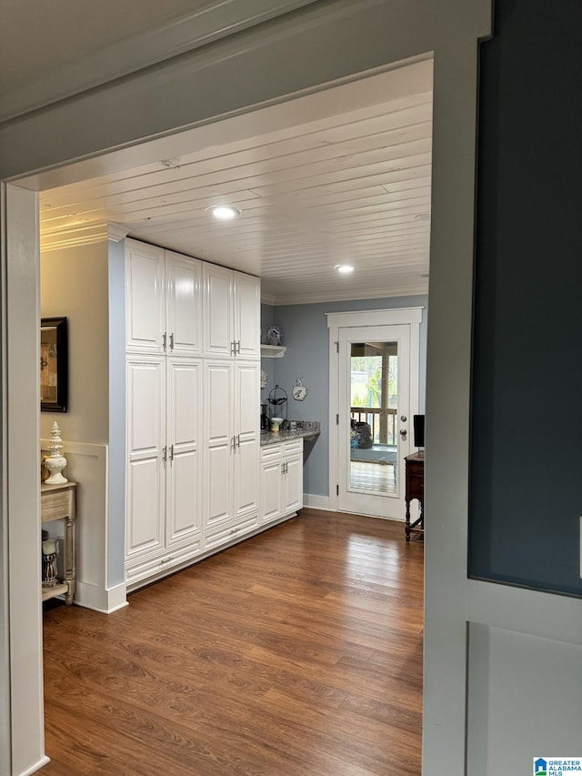 hallway with dark hardwood / wood-style flooring, ornamental molding, and white cabinets