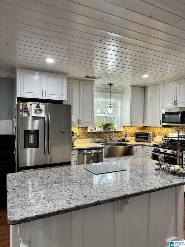 kitchen featuring hanging light fixtures, white cabinets, stainless steel appliances, light stone countertops, and backsplash