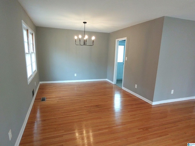 spare room with an inviting chandelier and light wood-type flooring