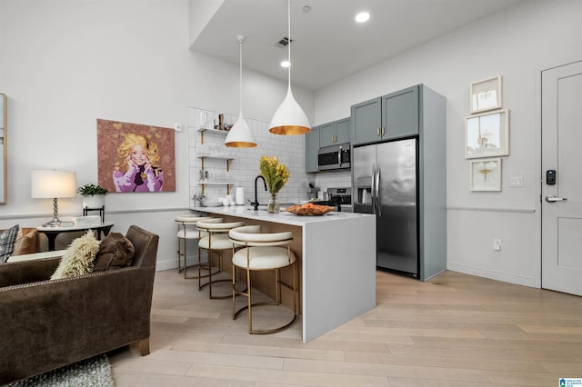 kitchen with a peninsula, open floor plan, hanging light fixtures, appliances with stainless steel finishes, and a kitchen bar