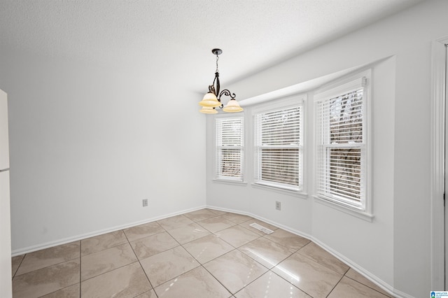 spare room featuring a wealth of natural light, a textured ceiling, a chandelier, and light tile patterned floors