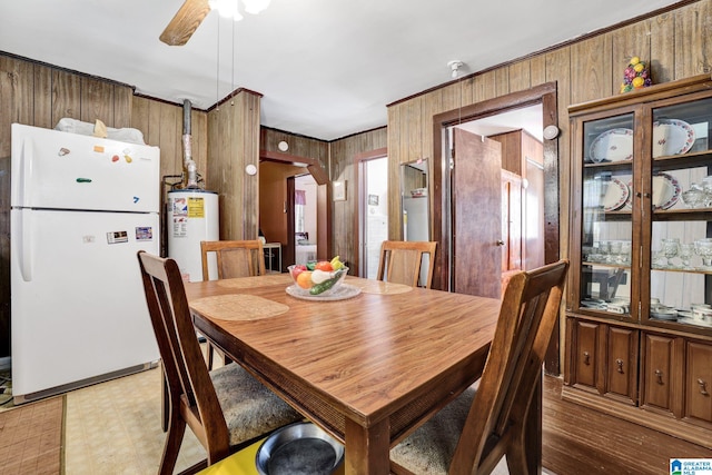 dining area featuring a ceiling fan, gas water heater, wood walls, and light floors