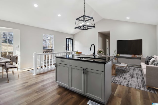 kitchen with dark wood-type flooring, lofted ceiling, sink, gray cabinetry, and a kitchen island with sink