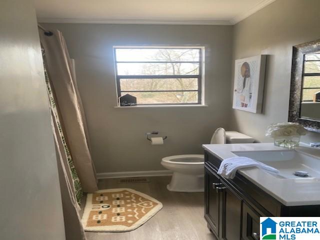 bathroom featuring toilet, wood finished floors, visible vents, vanity, and ornamental molding