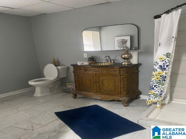 bathroom featuring a drop ceiling, a shower with shower curtain, toilet, marble finish floor, and vanity