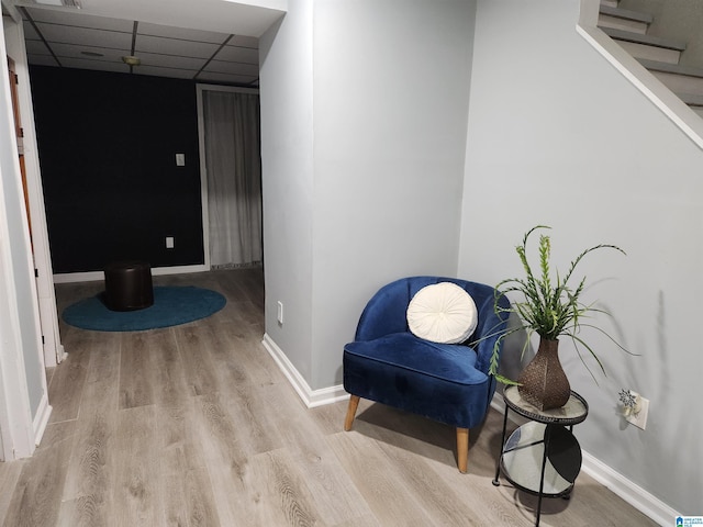 living area featuring baseboards, a drop ceiling, and light wood-style floors