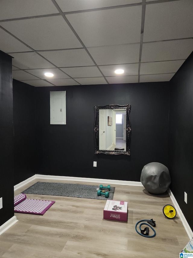 workout room featuring a drop ceiling, wood finished floors, electric panel, and baseboards