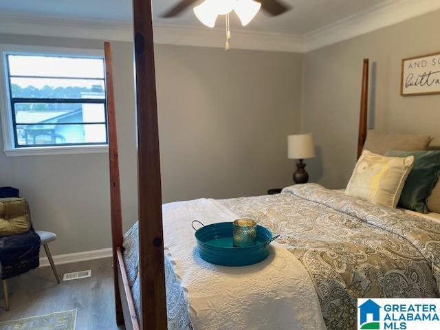 bedroom with ceiling fan, wood finished floors, visible vents, baseboards, and crown molding