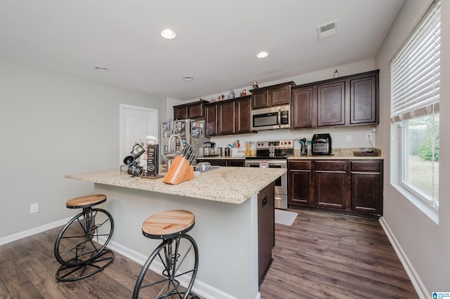 kitchen featuring stainless steel appliances, a kitchen island with sink, a breakfast bar area, and dark hardwood / wood-style flooring