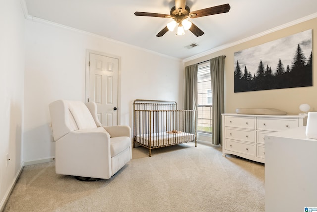 bedroom featuring a crib, ornamental molding, light colored carpet, and ceiling fan