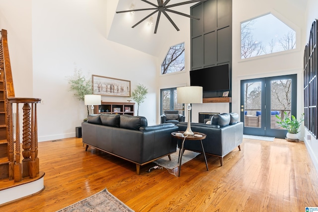 living area with light wood-style floors, a high ceiling, baseboards, and french doors