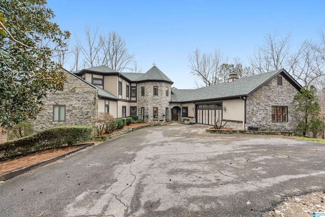 view of front of property with a garage, stone siding, driveway, stucco siding, and a chimney