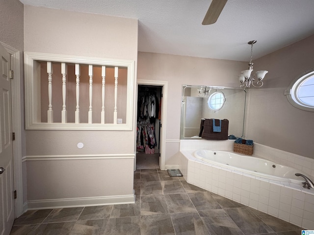 bathroom with ceiling fan with notable chandelier, a relaxing tiled tub, a textured ceiling, and a healthy amount of sunlight