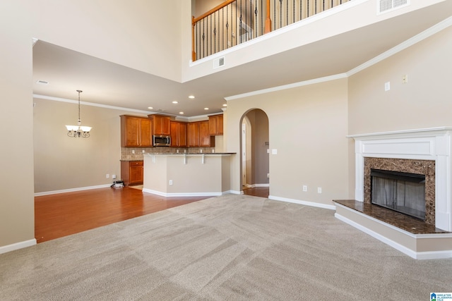 unfurnished living room featuring crown molding, light colored carpet, a notable chandelier, and a fireplace