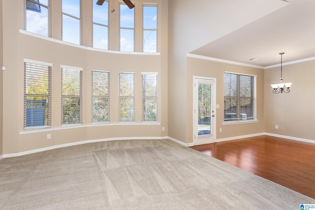 unfurnished living room featuring ornamental molding, wood-type flooring, ceiling fan with notable chandelier, and a towering ceiling