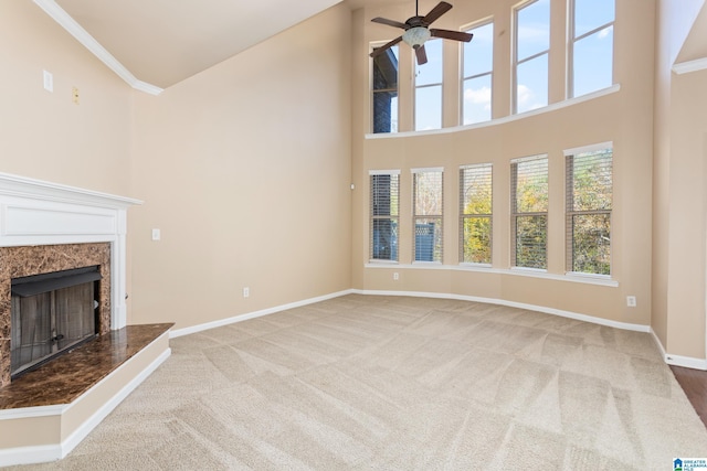 unfurnished living room featuring crown molding, carpet flooring, ceiling fan, a fireplace, and a high ceiling