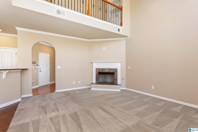 unfurnished living room with a towering ceiling, ornamental molding, a high end fireplace, and carpet